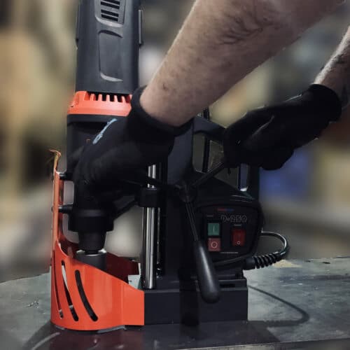 gloved hands operating a magnetic drill press